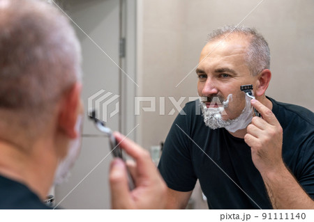 Middle aged handsome man shaving his beard in bathroom 91111140