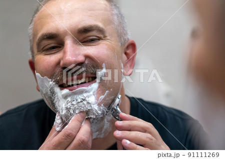 Middle aged handsome man shaving his beard in bathroom Middle aged handsome man shaving his beard in bathroom 91111269