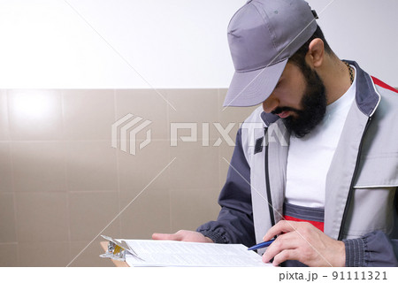Concentrated young technician wearing overall standing and taking notes 91111321