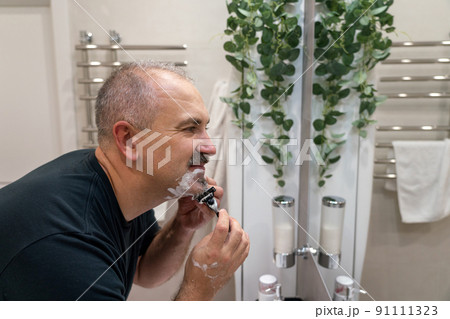 Man shaving with razor using foam in bathroom in the morning 91111323