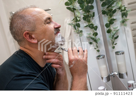Man shaving with razor using foam in bathroom in the morning 91111423
