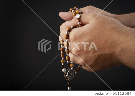 Folded hands of a young man holding a rosary during a pray isolated on black background 91112084