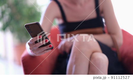 Woman sitting in chair with mobile phone in her hands closeup 91112527