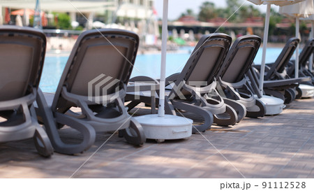 Many empty sun loungers and parasols standing near swimming pool 91112528