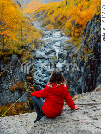 Autumnal trees and tourist woman sit on rock near river canyon. Mountain landscape with river 91112975