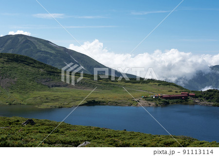 長野県富山県にある日本百名山の白馬岳への白馬大池付近の白馬大池山荘と雪渓と雲と青空の景色 91113114