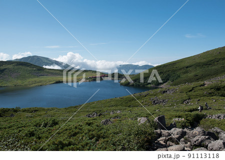 長野県富山県にある日本百名山の白馬岳への白馬大池付近の白馬大池山荘と雪渓と雲と青空と登山者の景色 91113118