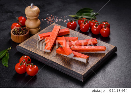Crab sticks on a cutting Board with a knife. On black concrete background 91113444