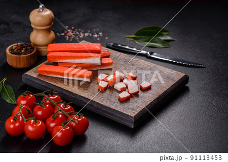 Crab sticks on a cutting Board with a knife. On black concrete background Crab sticks on a cutting Board with a knife. On black concrete background 91113453