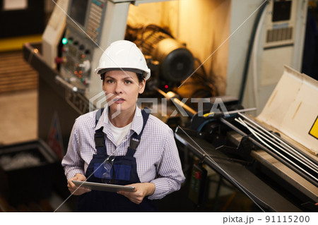 Portrait of content attractive woman in white hardhat standing by lathe and using tablet, she working in manufacturing industry Portrait of content attractive woman in white hardhat standing by lathe and using tablet, she working in manufacturing industry 91115200