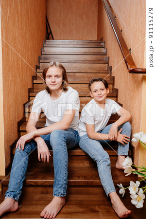 two brothers of a teenager in white T-shirts and jeans on a wooden staircase  91115279