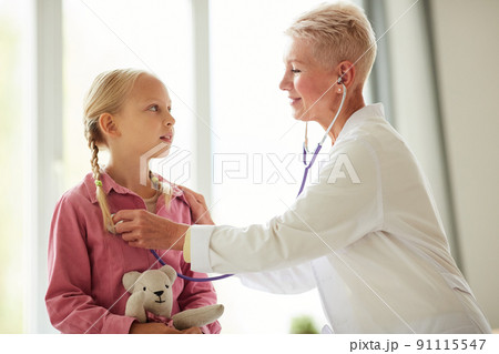 Content kind attractive female pediatrician listening to girls breathing with stethoscope while carrying out medical examination Content kind attractive female pediatrician listening to girls breathing with stethoscope while carrying out medical examination 91115547