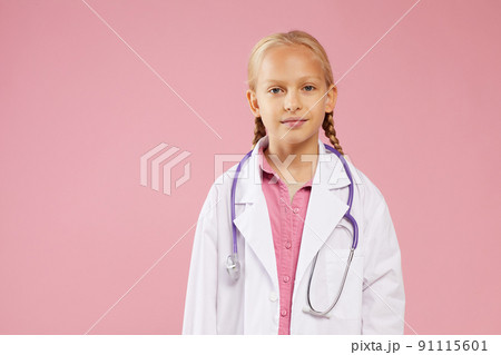 Content confident girl in lab coat wearing purple stethoscope around neck standing against pink background and looking at camera 91115601