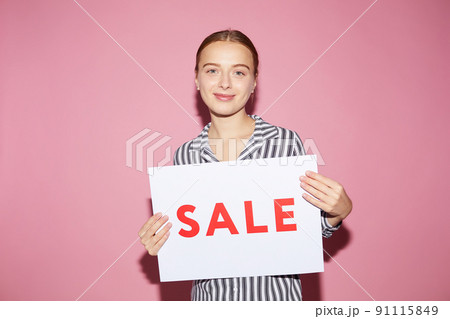 Portrait of smiling pretty girl in black and white shirt standing against pink wall and showing Sale tablet 91115849