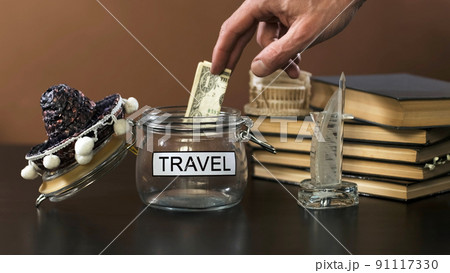 Man Trying to Save Some Money for Traveling, Putting Banknote into a Glass with Inscription Travel. Personal Finance Management and Savings Concept 91117330