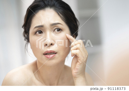 鏡に向かうアラフィフの女性　スキンケア　肌の悩み　イメージ 91118373