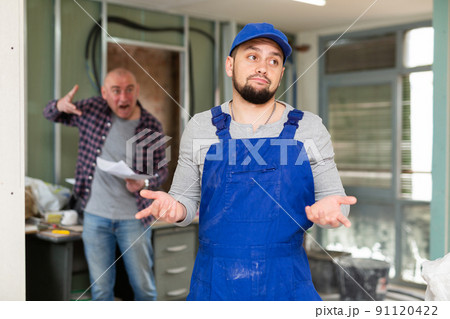 Perplexed builder in building under renovation with screaming customer Perplexed builder in building under renovation with screaming customer 91120422