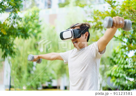 Active Asian sportsman doing a weight training exercise by using dumbbell and virtual reality - VR goggles platform for online training. The innovation of virtual reality or metaverse platform concept Active Asian sportsman doing a weight training exercise by using dumbbell and virtual reality - VR goggles platform for online training. The innovation of virtual reality or metaverse platform concept 91123581