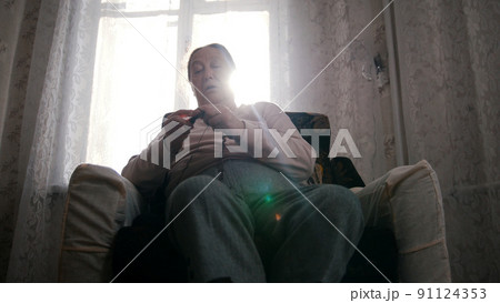 A portrait of an old woman sitting in the armchair and knitting 91124353