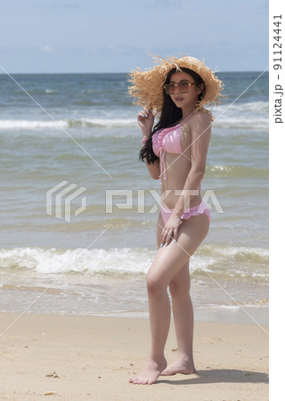 Girl in pinky bikini with hat relaxing and posing at beach 91124441