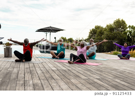 Multiracial senior friends with arms outstretched exercising on mats in yard against sky 91125433