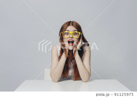 Surprised Caucasian woman sitting at table wearing yellow eyeglasses 91125975