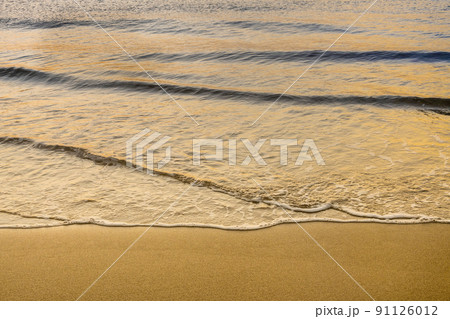 Close-up of calm ocean surf washing up onto beach at sunrise Close-up of calm ocean surf washing up onto beach at sunrise 91126012