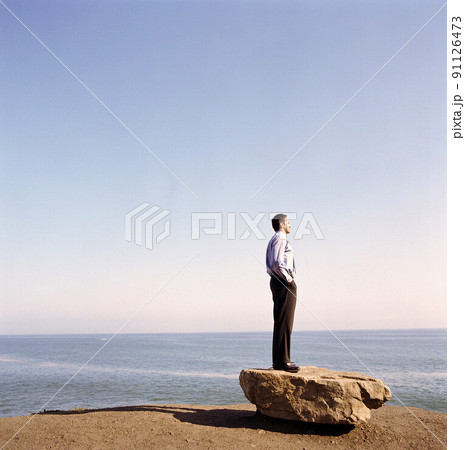USA, California, Point Mugu, Businessman standing on rock on beach USA, California, Point Mugu, Businessman standing on rock on beach 91126473