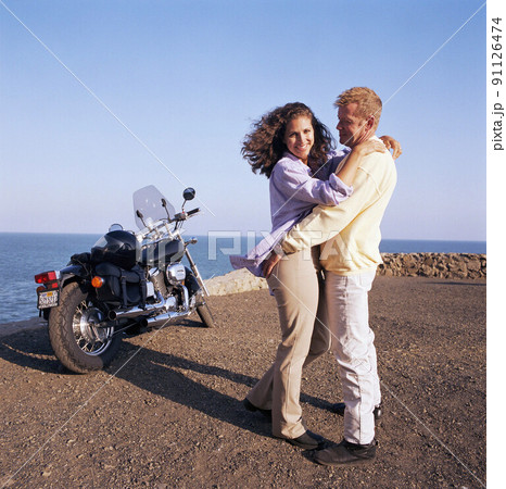 USA, California, Point Mugu, Couple hugging on coast next to motorcycle USA, California, Point Mugu, Couple hugging on coast next to motorcycle 91126474