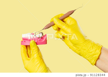 Dentist's hands with layout of the human jaw and dental instrument. 91128344