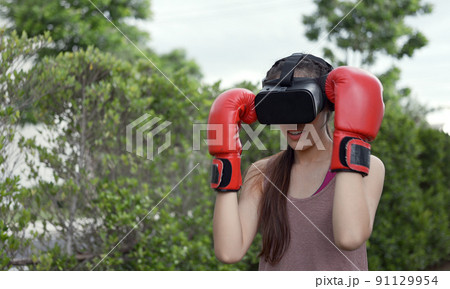 Young female wearing VR headset for working out boxing, aerobic training for boxing punch in virtual reality in simulation world. 91129954
