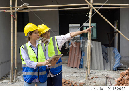 Young engineer in a construction helmet and safety vest explaining to foreman about the projects that are under construction. Work environment of engineers at the construction site of housing projects Young engineer in a construction helmet and safety vest explaining to foreman about the projects that are under construction. Work environment of engineers at the construction site of housing projects 91130065