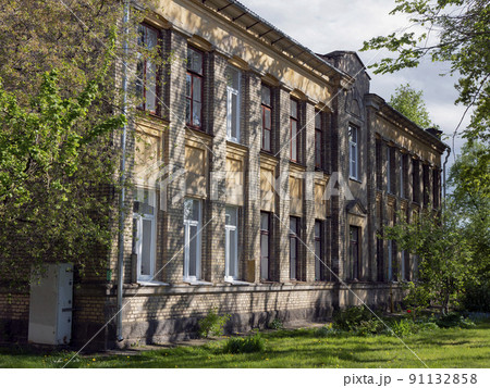 Two-story old brick building with a triangular pediment under bright sun 91132858
