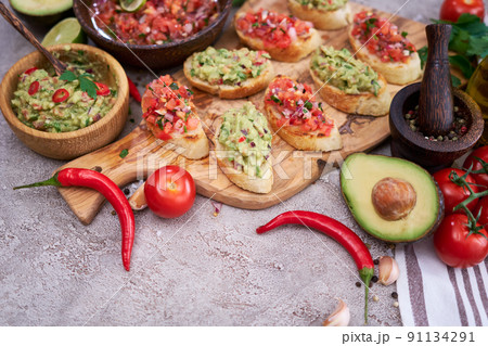 tasty salsa and guacamole bruschetta snacks at domestic kitchen on wooden cutting board 91134291