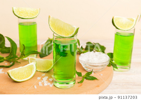 Sweet refreshing mint liqueur, with ice and mint leaves on table background, Shots with lime slice and mint flat lay Sweet refreshing mint liqueur, with ice and mint leaves on table background, Shots with lime slice and mint flat lay 91137203