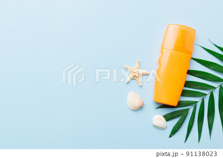 Sunscreen spray bottle. Bottle with sun protection cream and sea shells with tropical green leaf on color background, top view 91138023