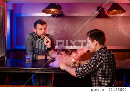 Vaping man holding a mod. A cloud of vapor at the vapebar. Vaping man holding a mod. A cloud of vapor at the vapebar. 91146892