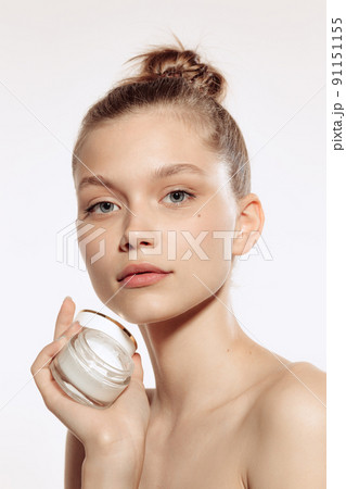 Half-length portrait of charming young girl without makeup holding cream bottle, posing isolated over white studio background. 91151155