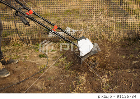 Male farmer plows the land with a cultivator. Agricultural machinery for tillage in the garden, combine harvester. Male farmer plows the land with a cultivator. Agricultural machinery for tillage in the garden, combine harvester. 91156734