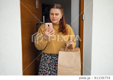 50s woman hands take a parcel by her self at home. Package on the floor by the door. Quarantine and isolation. Coronavirus concept 50s woman hands take a parcel by her self at home. Package on the floor by the door. Quarantine and isolation. Coronavirus concept 91156759