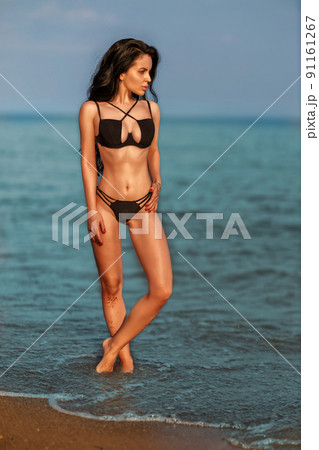 A beautiful young girl on the seashore in a black swimsuit enjoying her vacation A beautiful young girl on the seashore in a black swimsuit enjoying her vacation 91161267