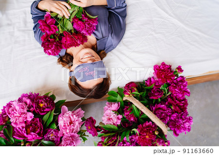 morning. a woman in pajamas and a bandage for sleeping in bed with a peonies. 91163660