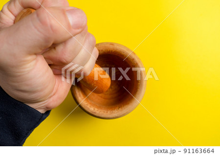 Man's hand with a wooden kitchen mortar prepared to make a sauce. Man's hand with a wooden kitchen mortar prepared to make a sauce. 91163664
