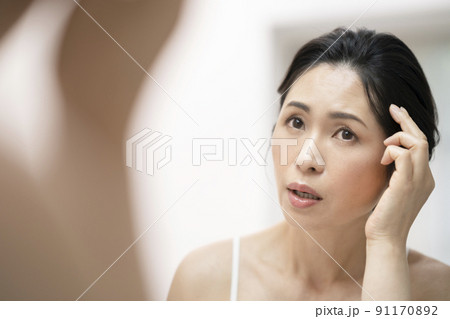 鏡を見ながら生え際を気にするアラフィフの女性 91170892