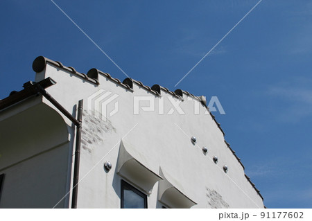 青空に映える珍しい形状の美しいオシャレでかわいい白亜のしっくいのプロヴァンス風住宅の妻壁 91177602