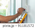 Electrician using a digital meter to measure the voltage at a wall socket. 91181572