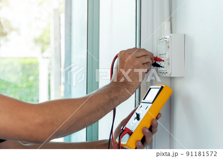Electrician using a digital meter to measure the voltage at a wall socket. Electrician using a digital meter to measure the voltage at a wall socket. 91181572