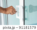 Man's hand opening a glass door with a key. 91181579