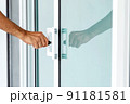 Man's hand opening a glass door with a key. 91181581