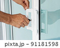Man's hand opening a glass door with a key. 91181598